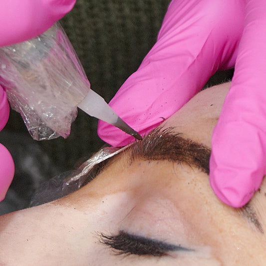 PMU artist stretching brow skin while applying pigment with a machine.