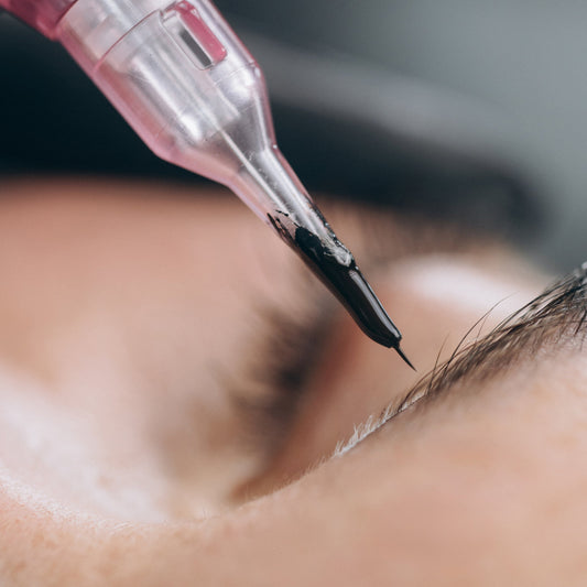Close-up of a pigment-filled PMU cartridge poised over a client’s eyebrow.